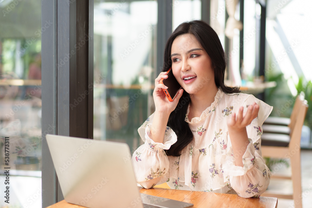 Young woman using smartphone at table with laptop in coffee shop.