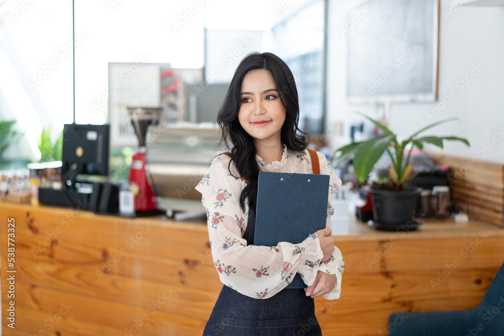 Happy Asian woman in an apron standing near a bar counter coffee shop, Small business owner, restaur