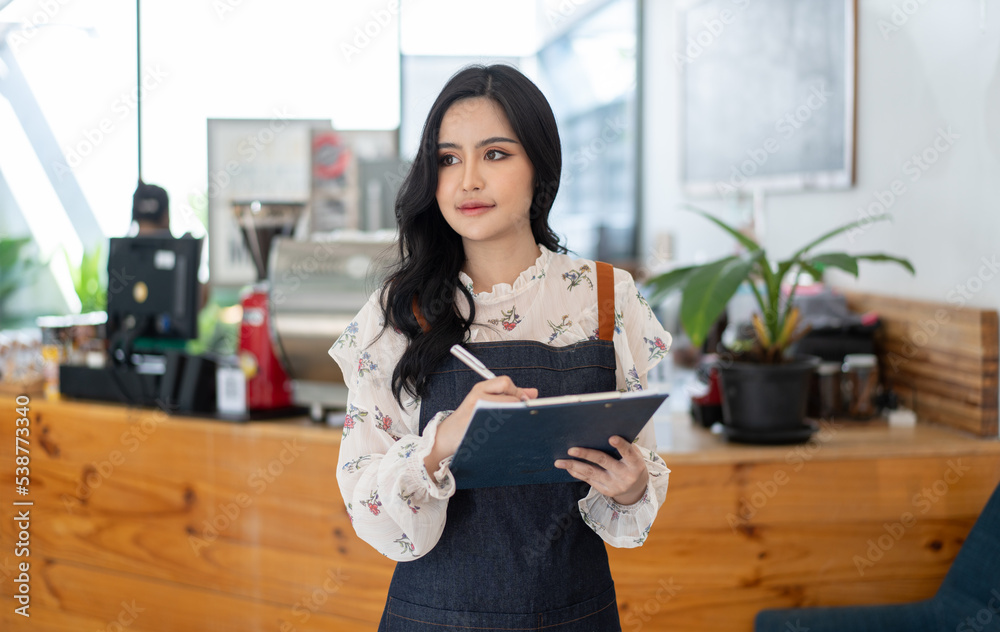 Happy Asian woman in an apron standing near a bar counter coffee shop, Small business owner, restaur