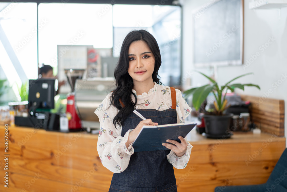 Happy Asian woman in an apron standing near a bar counter coffee shop, Small business owner, restaur