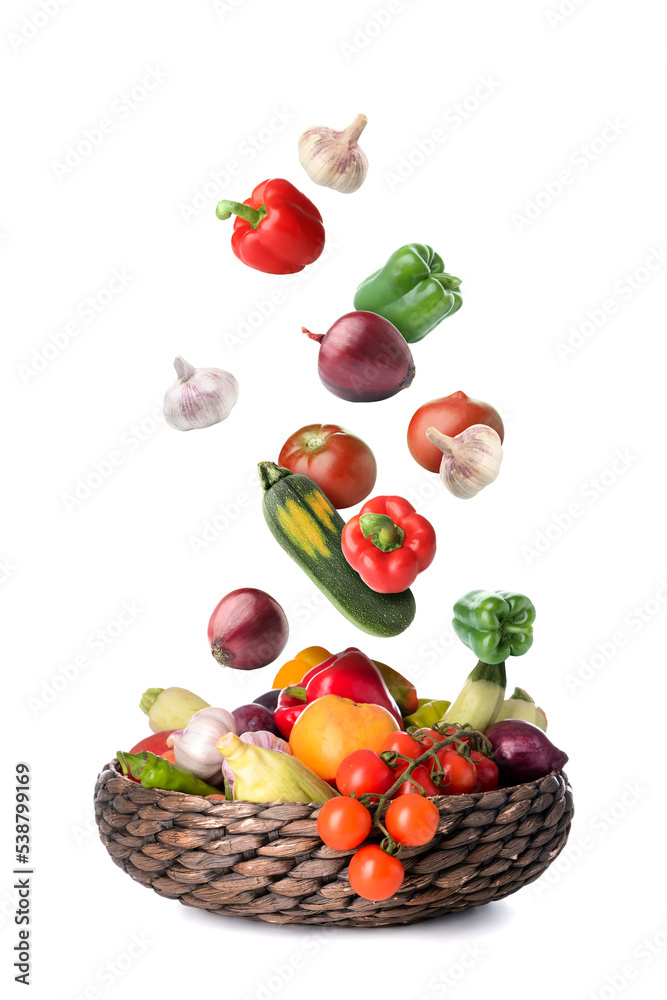 Many healthy vegetables falling into wicker basket on white background