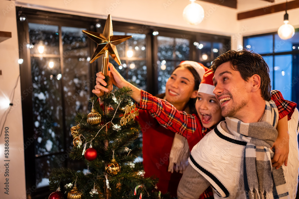 Caucasian couple and young daughter decorating Christmas tree at home.