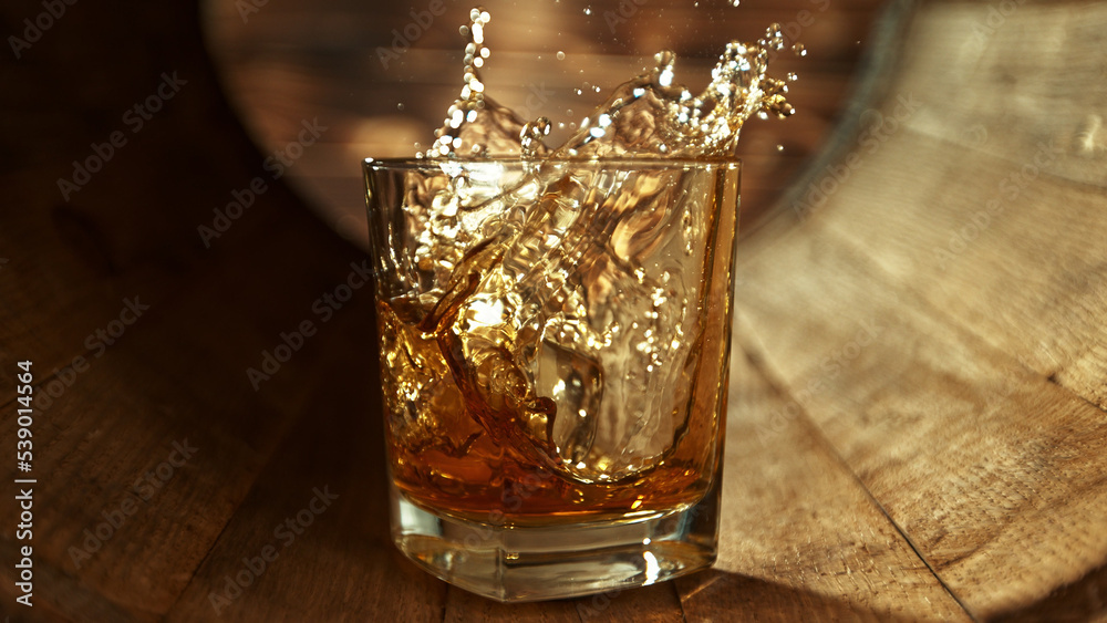 Ice cube falling into glass of whisky in wooden barrel.