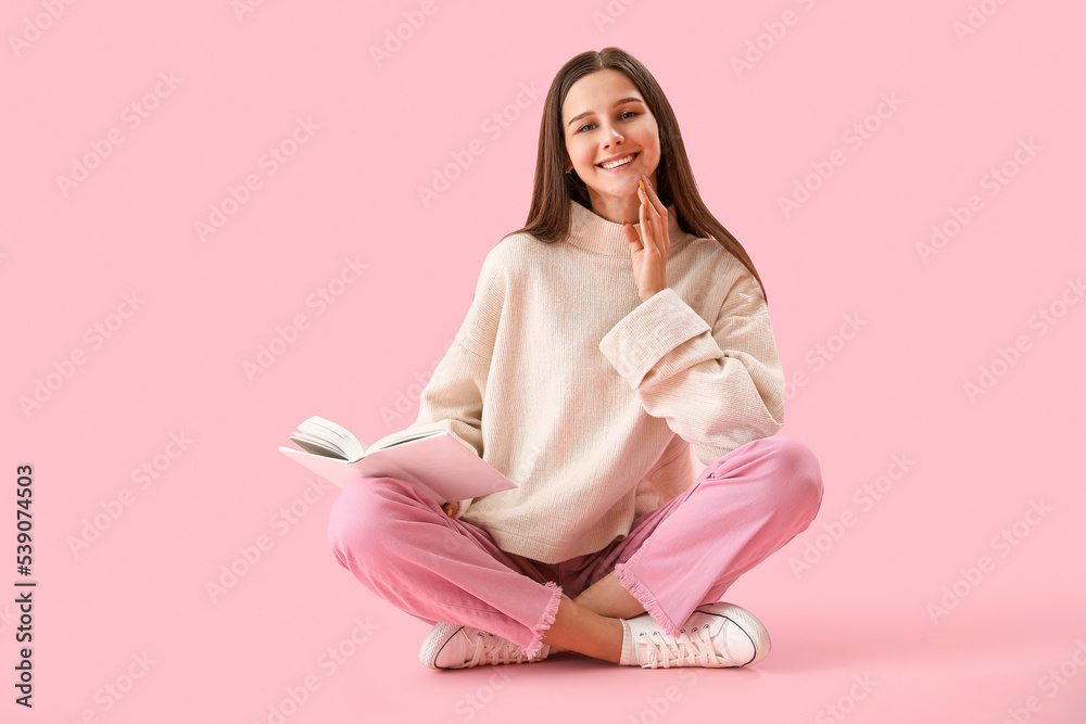 Beautiful woman with book sitting on pink background