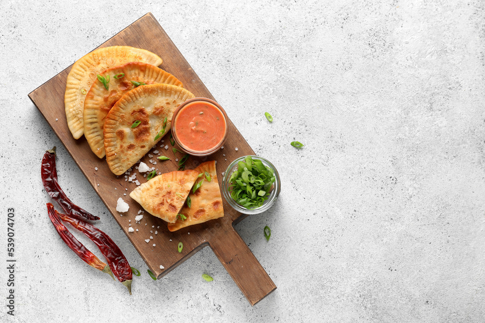 Wooden board with tasty chebureks, sauce, green onion and chili peppers on light background