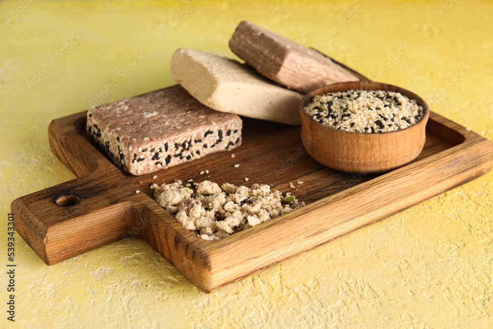 Wooden board with bowl of sesame seeds and sweet halva on color background