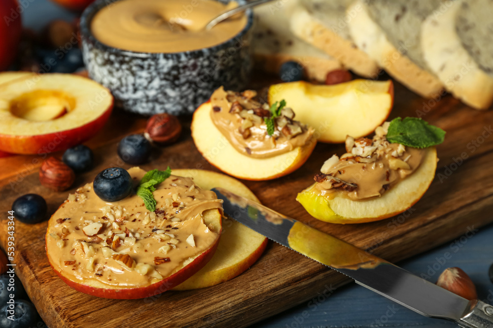 Wooden board of tasty apple rounds and wedges with nut butter, closeup