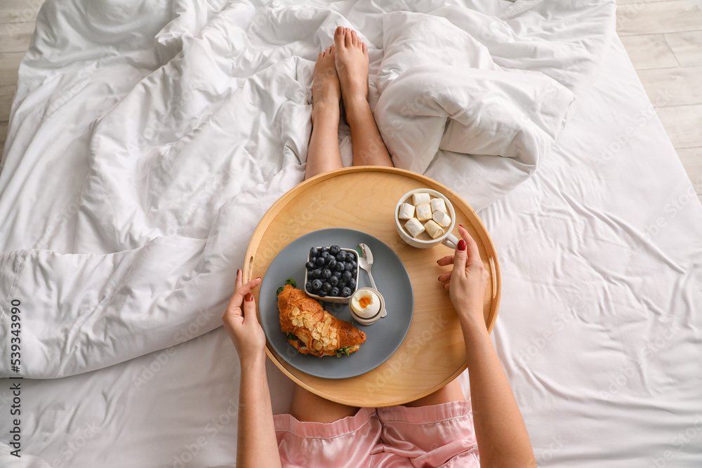 Woman holding wooden tray with tasty breakfast on bed