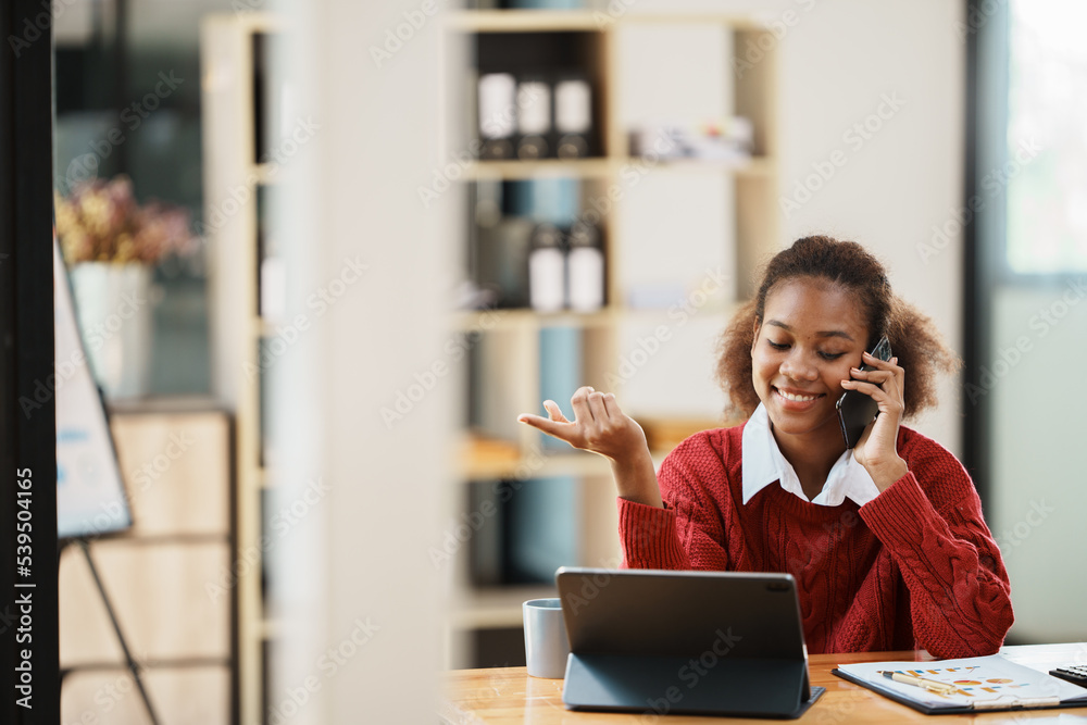 Focused young african american businesswoman or student looking at laptop holding book learning, ser