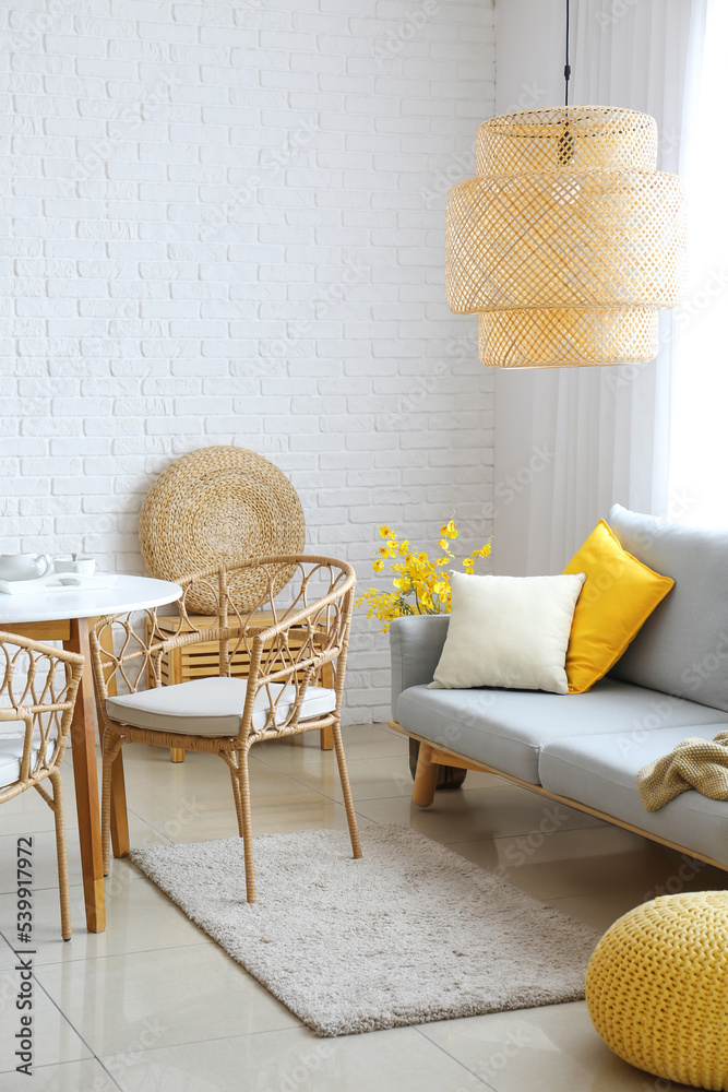 Dining table and comfortable sofa near white brick wall in room interior