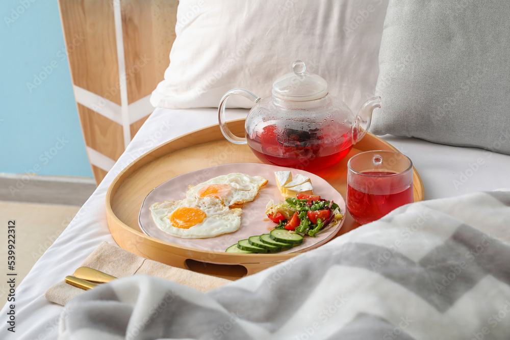 Wooden tray with tasty fried eggs and tea on bed