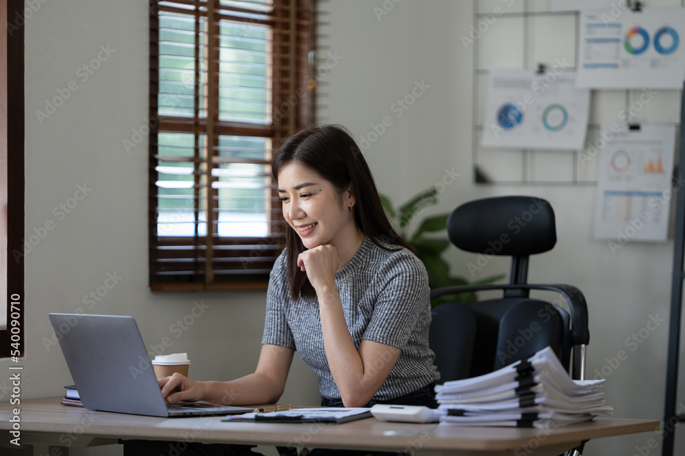 Beautiful young Asian businesswoman smiling holding a coffee mug and laptop working at the office.