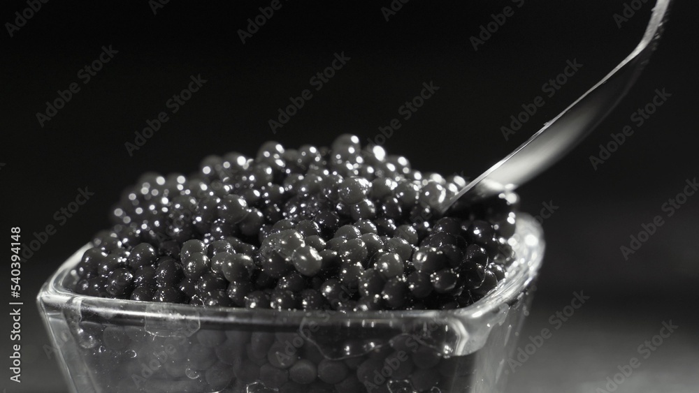 A man scoops up a delicious black caviar from a transparent bowl with a spoon. Delicious seafood, go