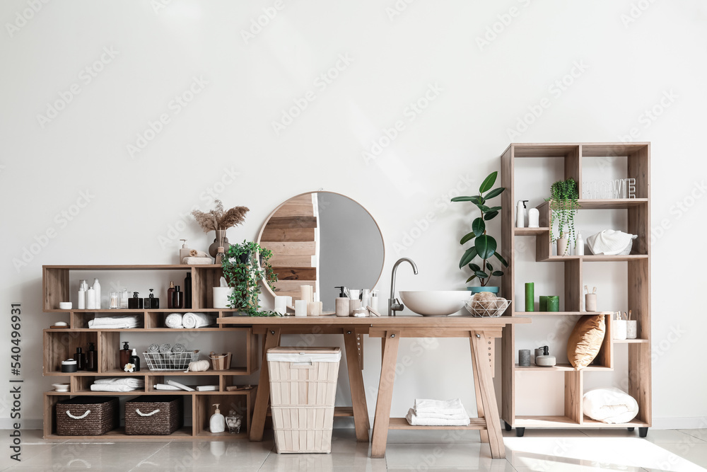 Stylish interior of bathroom with modern sink and shelf units with bath accessories near white wall