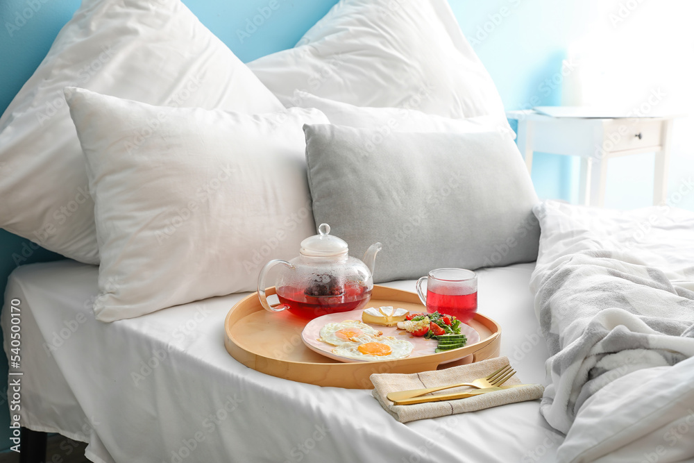 Wooden tray with tasty breakfast on comfortable bed