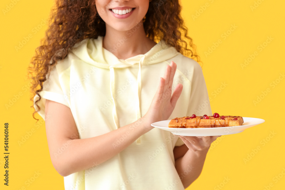 Young African-American woman refusing from pastry on yellow background. Diet concept