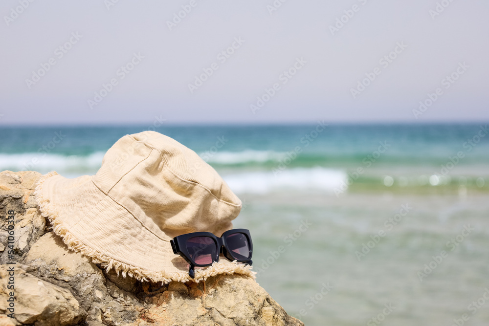 Stylish bucket hat and sunglasses on rock near sea, closeup