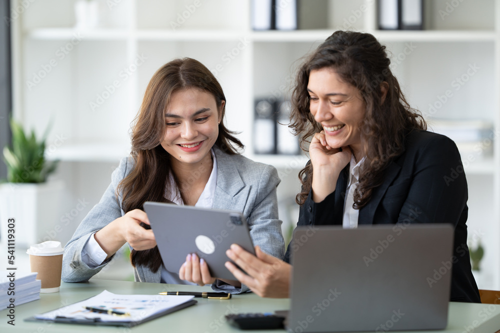 Cheerful young female entrepreneur browsing tablet and laptop at workplace in office.