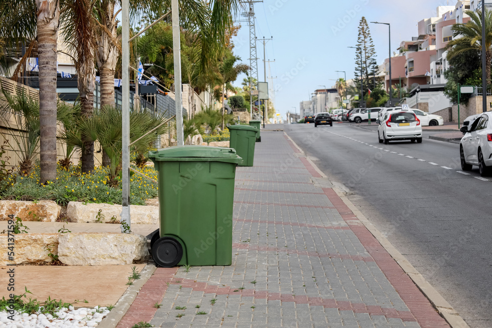 Green garbage containers near road in city