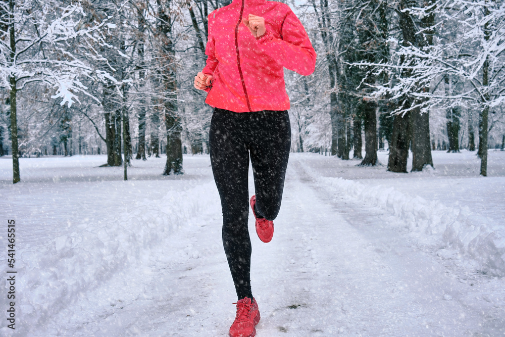 Running woman, girl runner on snow in park in winter sunny day.