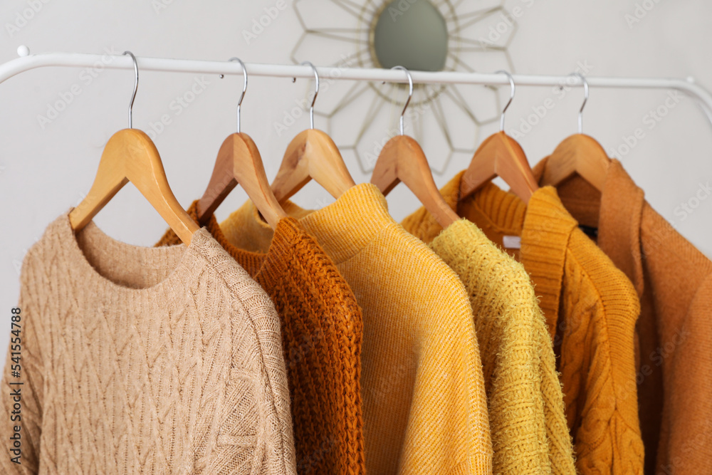 Rack with female warm sweaters near light wall, closeup