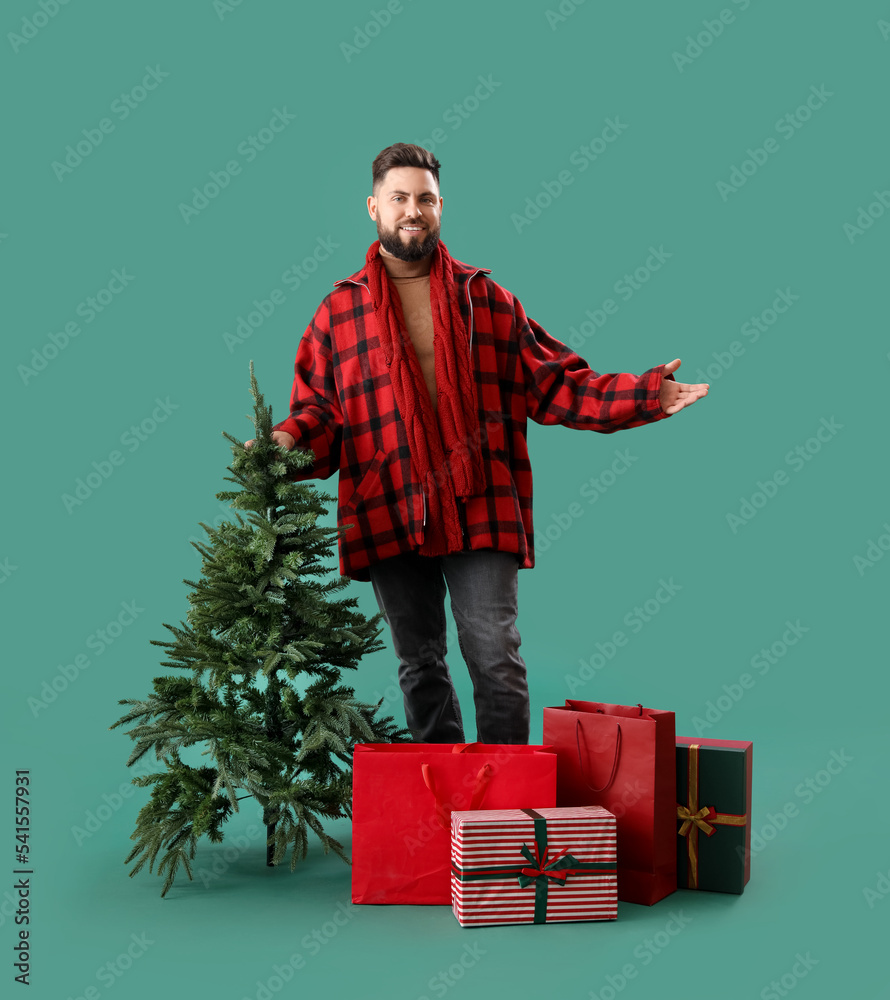 Handsome man with Christmas tree, shopping bags and gifts on green background