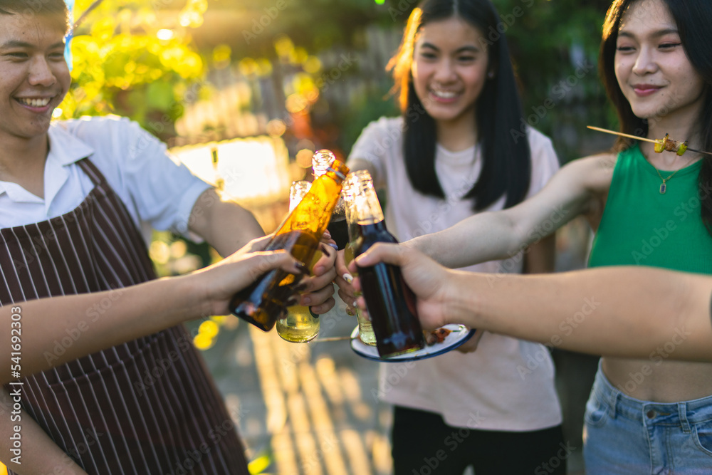 A group of Asian friends clinks a wine bottle during a party barbecue.