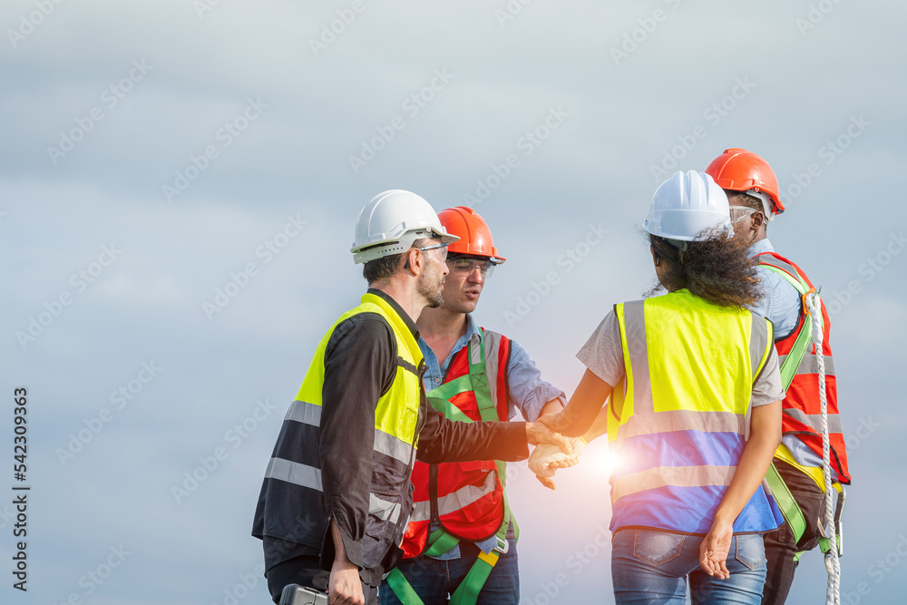 戴着防护帽的建筑工人在屋顶上的太阳能电池上工作时正在握手