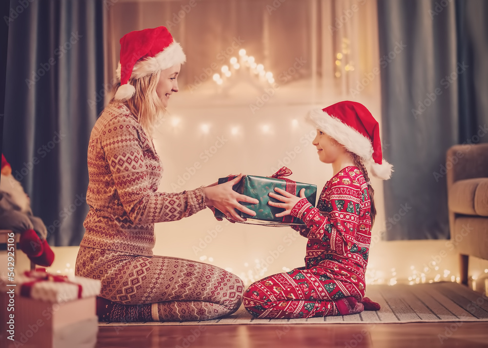 Mom and daughter indoors giving present box each other in Christmas eve.