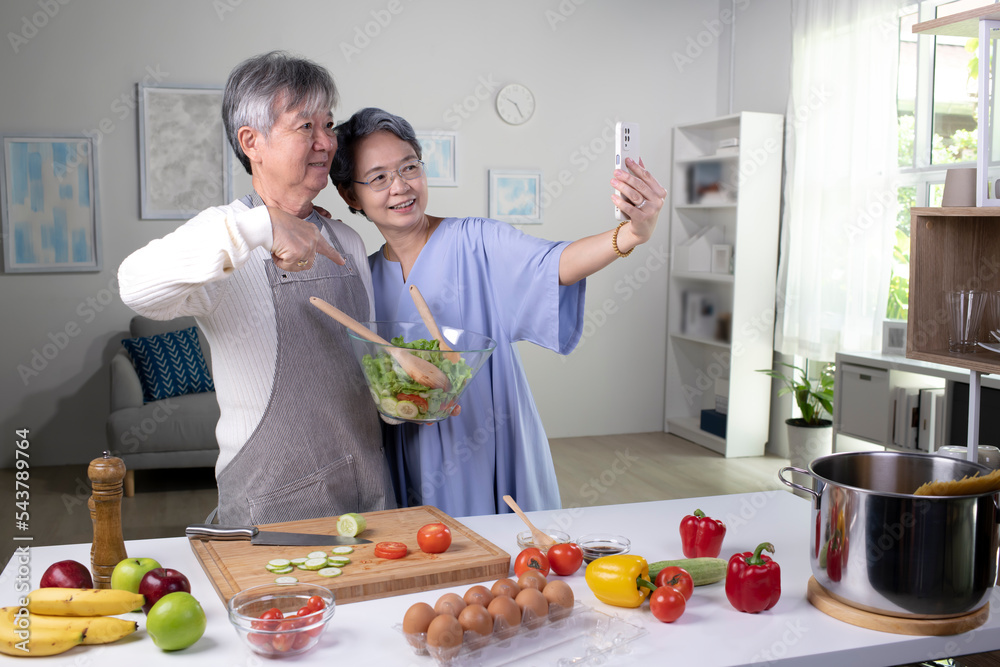 快乐的亚洲老年夫妇在做饭和自拍时看起来很开心。老夫妇在做饭