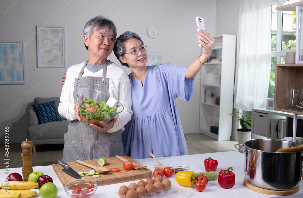 Happy Asian senior couple looking happy while cooking and taking selfie. Old couple preparing meal s