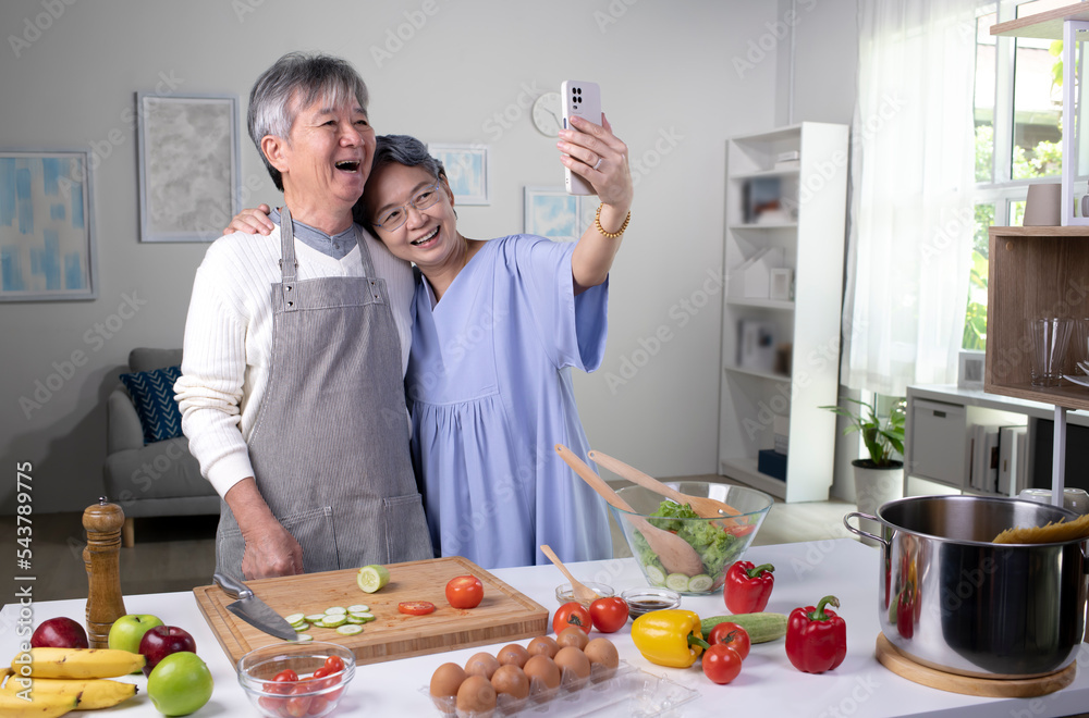 快乐的亚洲老年夫妇在做饭和自拍时看起来很开心。老夫妇在做饭