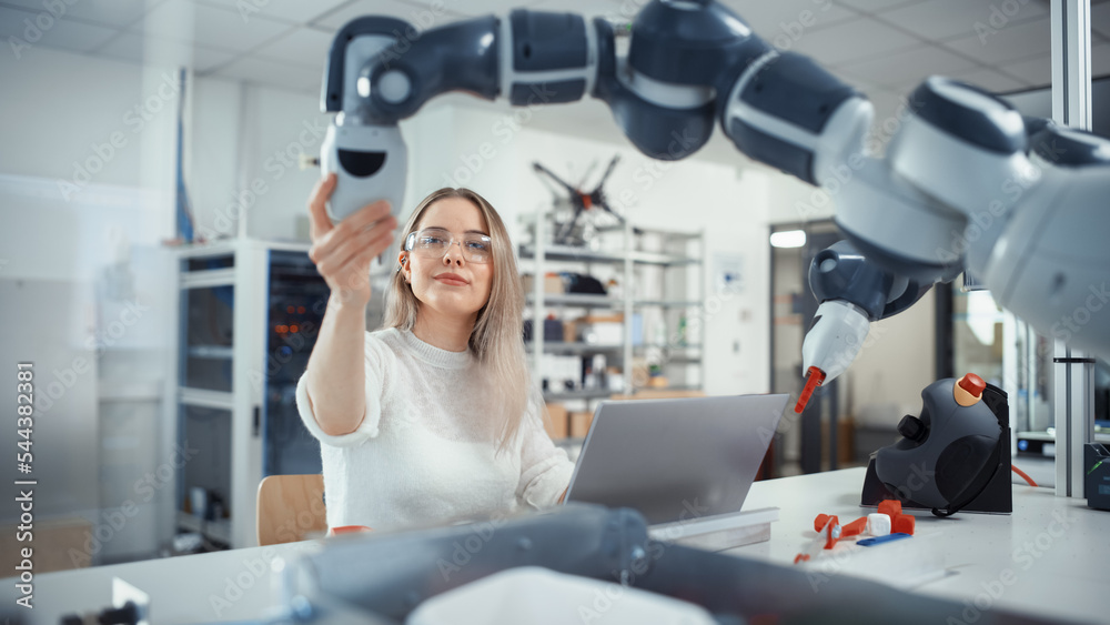 Female Automation Engineer Types on Laptop and Moves Bionic Claw At the Factory. Modern and Futurist