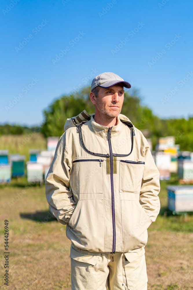 Summer honey farming apiarist. Man in protective beekeeping suit in apiary.