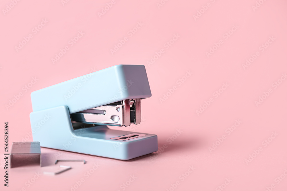 Office stapler and staples on pink background