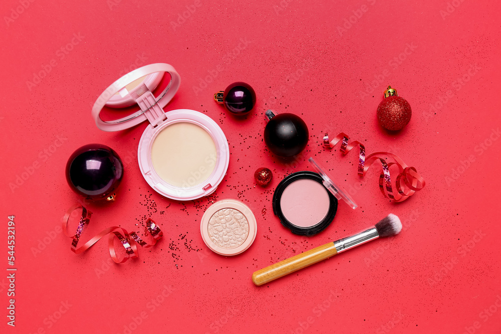 Makeup products with Christmas balls and serpentine on red background