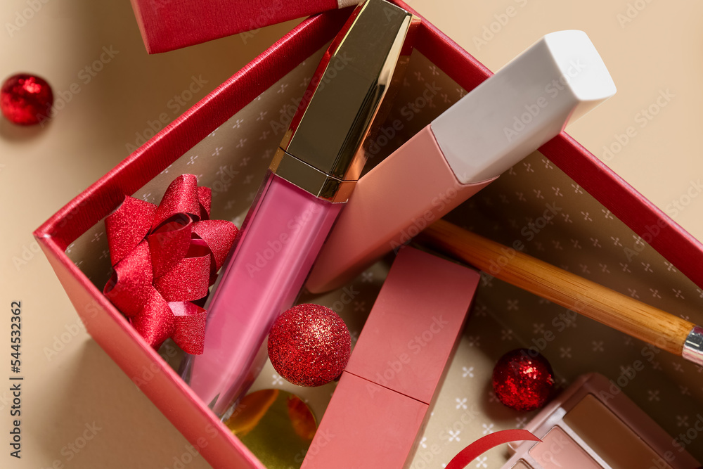 Gift box with makeup products and Christmas decor on beige background