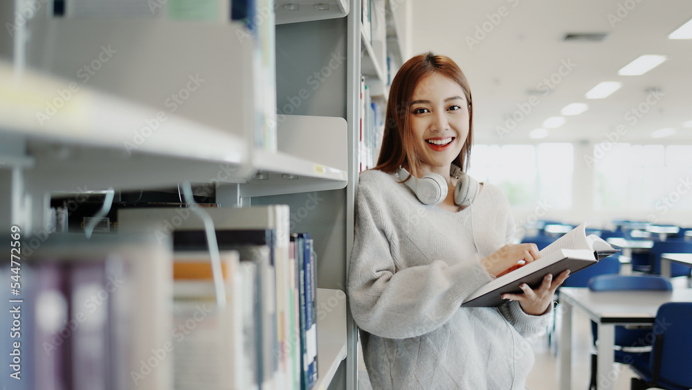 穿着毛衣的亚洲年轻学生女孩在大学图书馆的书架上找书