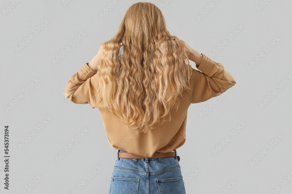 Woman touching blonde curly hair on light background