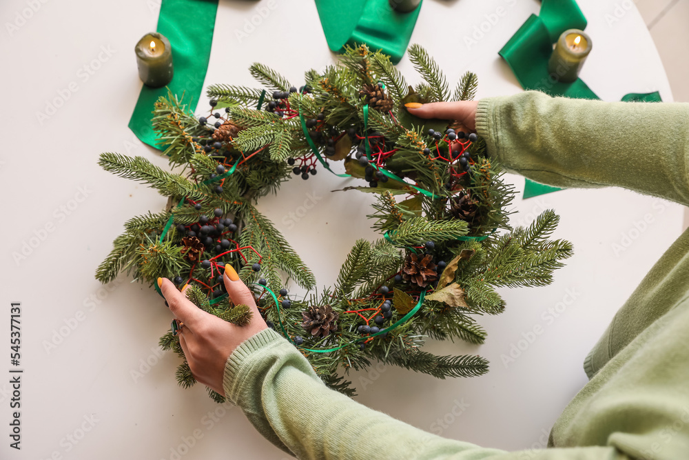 Woman making Christmas wreath at white table, closeup