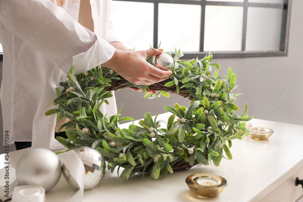 Woman making Christmas mistletoe wreath with ball at white table, closeup