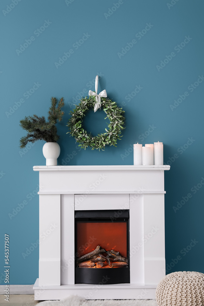 Fireplace with fir branches in vase, candles and Christmas mistletoe wreath on blue wall