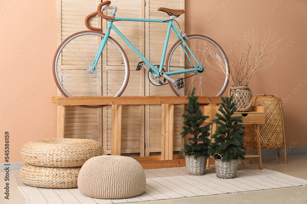 Interior of living room with bicycle, shelf and small fir trees