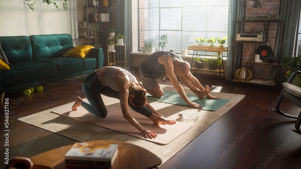 Athletic Young Couple Exercising Together, Stretching and Doing Yoga in the Morning in Sunny Room of