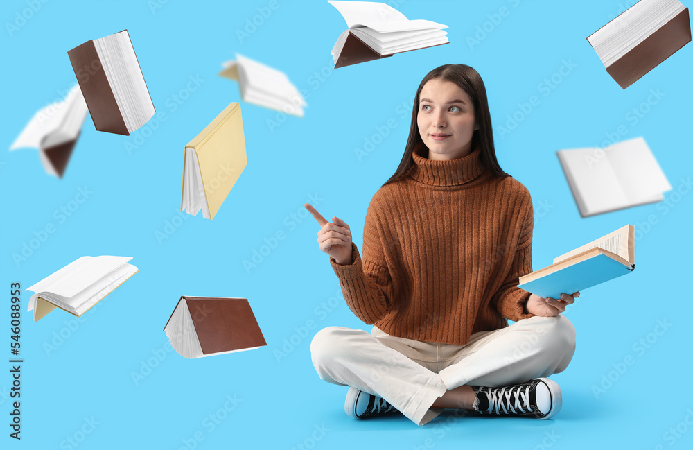 Pretty young woman pointing at many flying books on light blue background