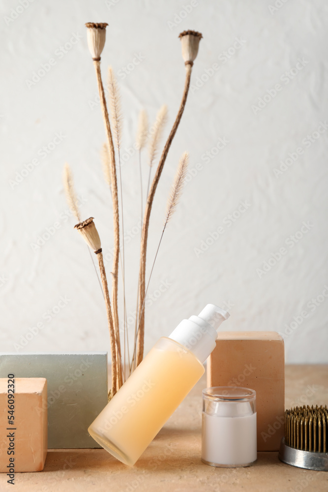 Cosmetic products with ikebana and decor on table near white wall