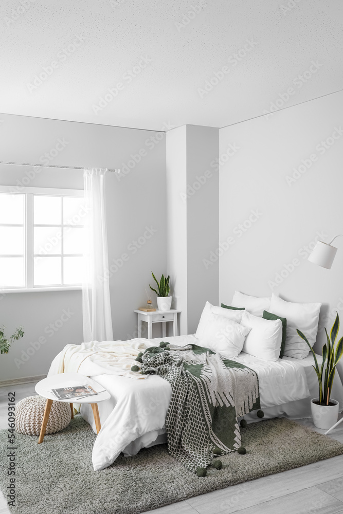 Interior of light room with big bed, houseplants and tables