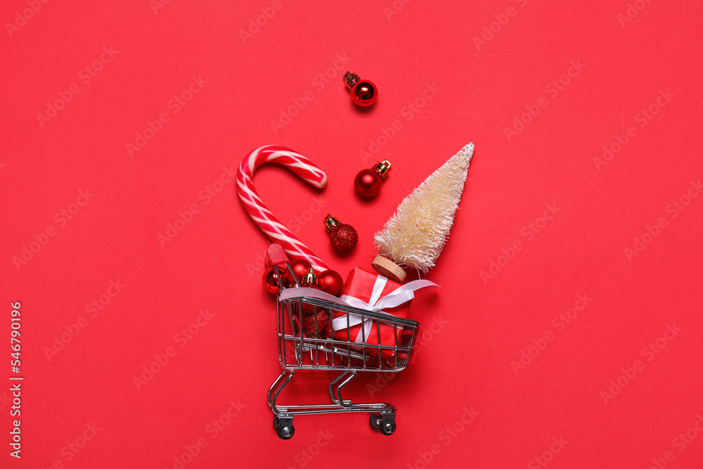 Shopping cart with Christmas balls, fir tree and candy cane on red background