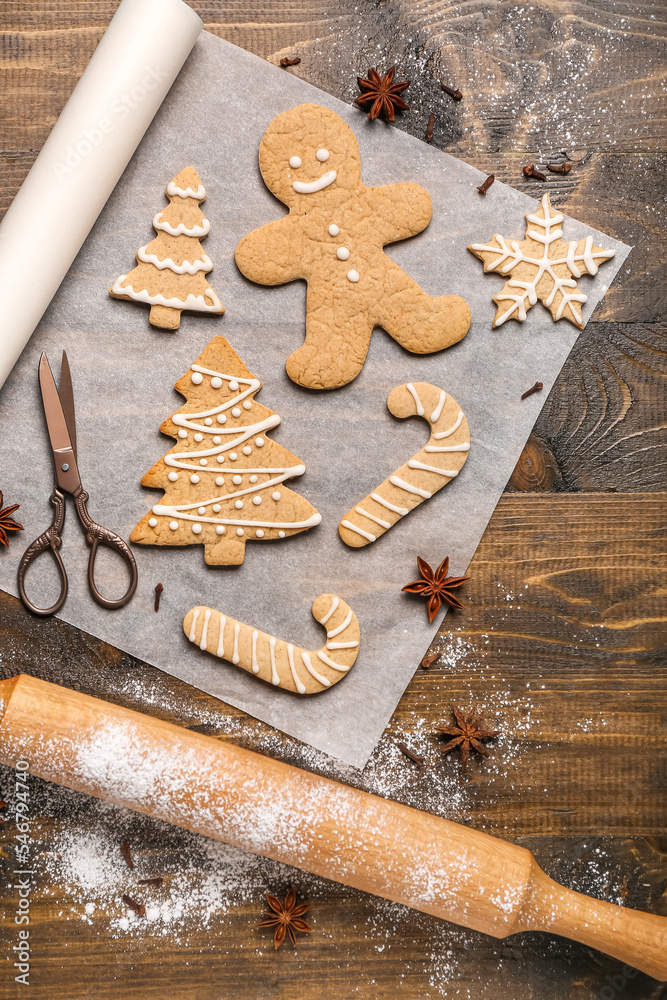 Baking paper with tasty Christmas cookies, scissors, rolling pin and spices on wooden background