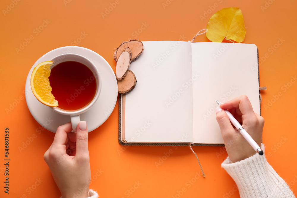 Female hands with blank notebook, pen and cup of tea on color background